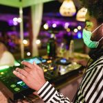 Young african DJ man mixing music at club outdoor while wearing safety face mask for coronavirus outbreak