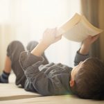 Little boy lying on back and reading a book