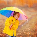 Happy girl with rainbow umbrella in autumn park